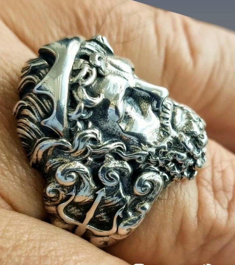 A silver Poseidon ring on a man's finger with the shank decorated with his trident