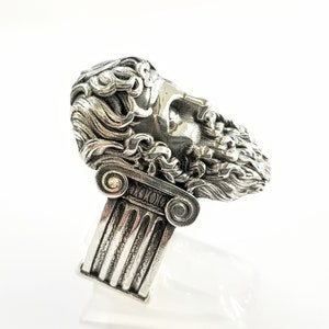 A large silver ring featuring the powerful figure of Zeus, the king of the gods, intricately carved atop a sturdy band.  Flanked by majestic Greek columns on each side, this bold statement piece exudes strength, sophistication, and timeless appeal.