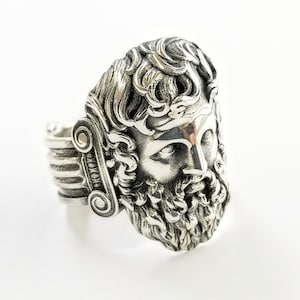 A large silver ring featuring the powerful figure of Zeus, the king of the gods, intricately carved atop a sturdy band.  Flanked by majestic Greek columns on each side, this bold statement piece exudes strength, sophistication, and timeless appeal.