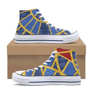 May include: High-top canvas sneakers with a vibrant geometric design. The shoes feature a blue and gold pattern with white laces and soles. The design includes red and blue triangles and lines. The sneakers are displayed on a brown cardboard box.