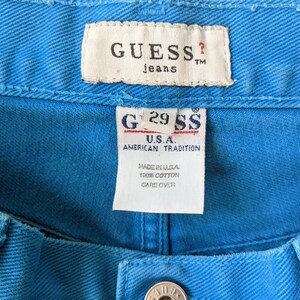 Puede incluir: Una etiqueta de mezclilla azul Guess con el texto "GUESS? jeans TM" y "G29 SS U.S.A. AMERICAN TRADITION MADE IN U.S.A. 100% COTTON CARE OVER"