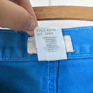 Puede incluir: Una etiqueta de cuidado blanca unida a un par de pantalones vaqueros azules. La etiqueta tiene el texto "STYLE 43924A CUT 52430" e instrucciones para lavar a m&aacute;quina por separado en agua fr&iacute;a, sin lej&iacute;a y secar en secadora a baja temperatura.