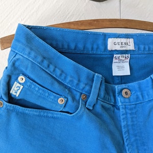 Puede incluir: Un par de pantalones vaqueros azules de mezclilla con una etiqueta de Guess. Los pantalones tienen un lavado azul claro y est&aacute;n hechos de 100% algod&oacute;n.