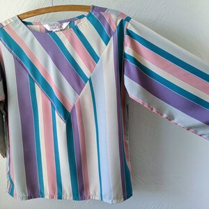 May include: A striped blouse with a teal, purple, pink, and white color scheme. The blouse has a round neckline and three-quarter sleeves.