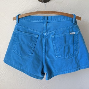 Puede incluir: Pantalones cortos de mezclilla azul con un bolsillo trasero y una etiqueta Guess.