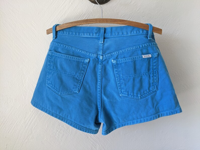 Puede incluir: Pantalones cortos de mezclilla azul con un bolsillo trasero y una etiqueta Guess.