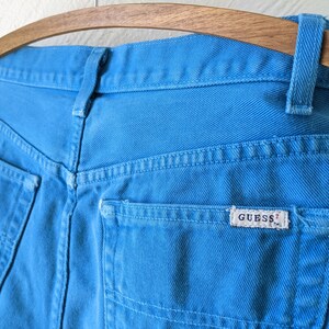 Puede incluir: Un par de pantalones vaqueros azules con un bolsillo trasero que tiene una etiqueta blanca "GUESS?"