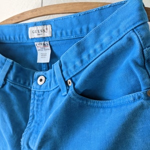 Puede incluir: Un par de pantalones vaqueros azules con una etiqueta de Guess Jeans. Los vaqueros tienen un lavado azul claro y un estilo cl&aacute;sico de cinco bolsillos.