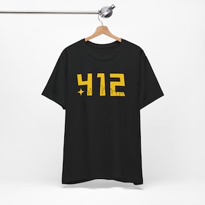 Peut inclure: T-shirt noir avec un motif jaune représentant le nombre 412 et une petite étoile avec un design de skyline.