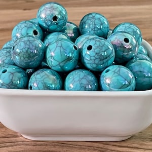 May include: A bowl filled with turquoise blue round beads with a crackled finish. The beads have a slight iridescent sheen.