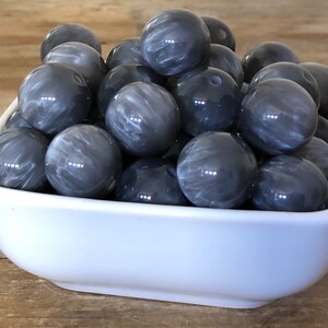 May include: A bowl filled with gray and white marbled round beads. The beads are smooth and shiny.