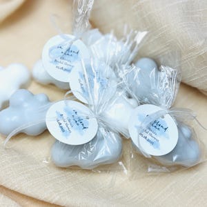 May include: Cloud-shaped favours wrapped in clear cellophane bags with blue and white watercolour tags that say "on cloud nine" and "Olivia's Bridal Shower" with the date 05.18.2025.
