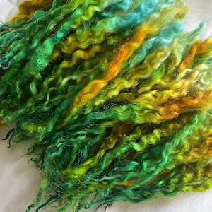 May include: Close-up of colorful, textured yarn in shades of green, yellow, and orange. The yarn has a curly, wavy texture, and is likely used for fiber art projects like knitting or crochet.