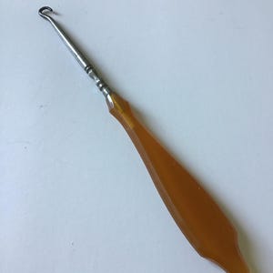 May include: A metal shoe horn with a brown plastic handle. The handle is shaped like a teardrop.