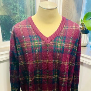 May include: A burgundy, green, and gold plaid v-neck sweater. The sweater is made of a soft, knit fabric and has a relaxed fit.