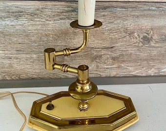 May include: A brass candlestick lamp with a white ceramic candle and a white light bulb. The lamp has a yellow base with a gold trim and a switch on the side. The lamp is on a white surface.