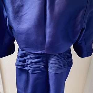 May include: A royal blue dress with a matching bolero jacket. The dress has a fitted bodice and a skirt with pleats at the back.