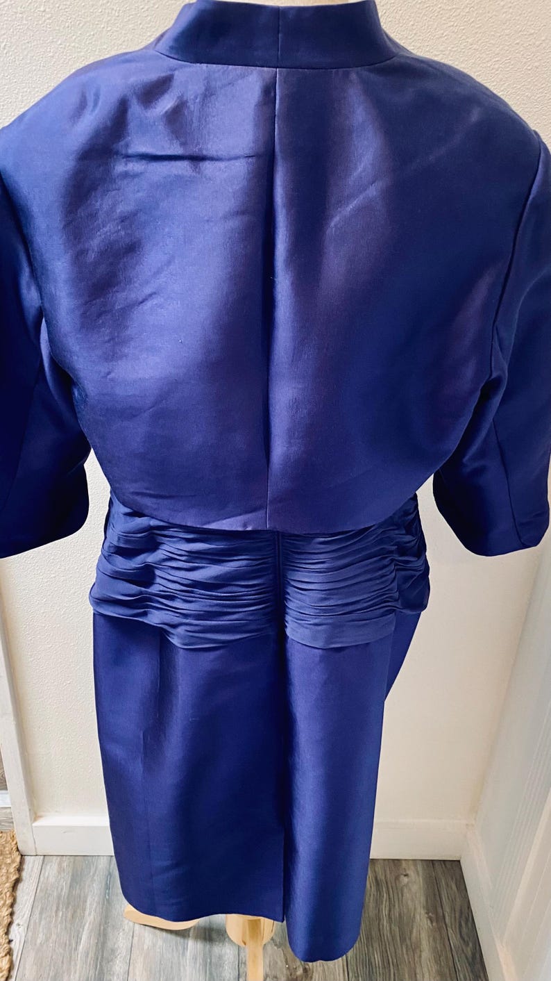 May include: A royal blue dress with a matching bolero jacket. The dress has a fitted bodice and a skirt with pleats at the back.