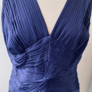 May include: A sleeveless, deep blue, pleated dress with a V-neckline. The dress is made of a silky fabric and has a fitted silhouette.