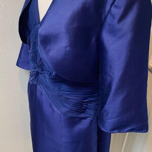May include: A royal blue dress with a matching jacket. The dress has a fitted bodice with a pleated skirt and a V-neckline. The jacket has a shawl collar and three-quarter sleeves.