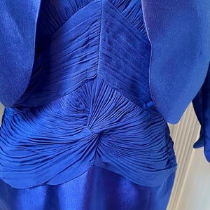May include: A royal blue dress with a matching jacket. The dress has a pleated bodice and a smooth skirt. The jacket has a short, cropped style.