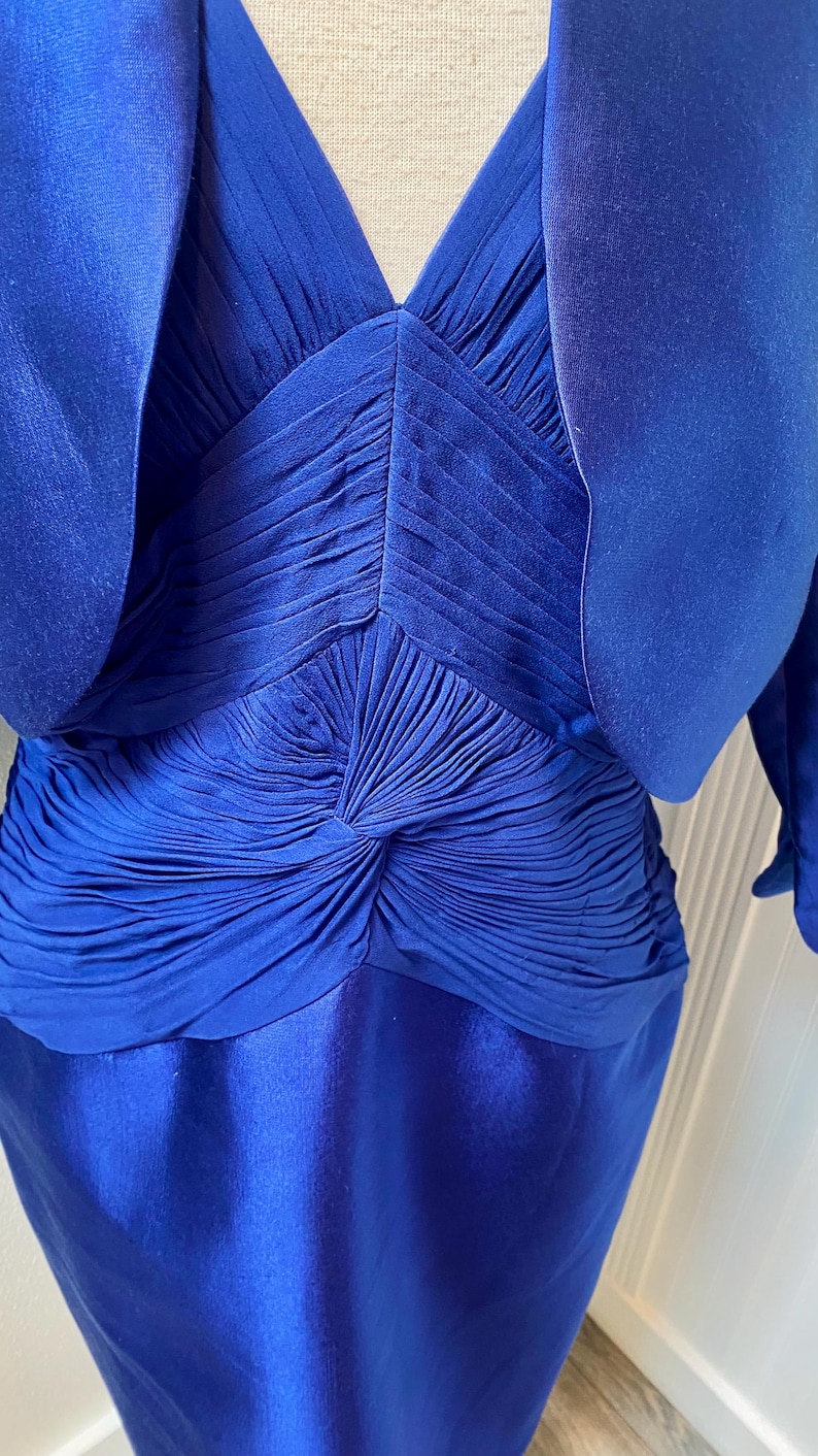 May include: A royal blue dress with a matching jacket. The dress has a pleated bodice and a smooth skirt. The jacket has a short, cropped style.