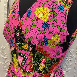 May include: A sleeveless pink dress with a floral print in shades of green, blue, yellow, red, and black. The dress has a V-neckline and a fitted bodice.