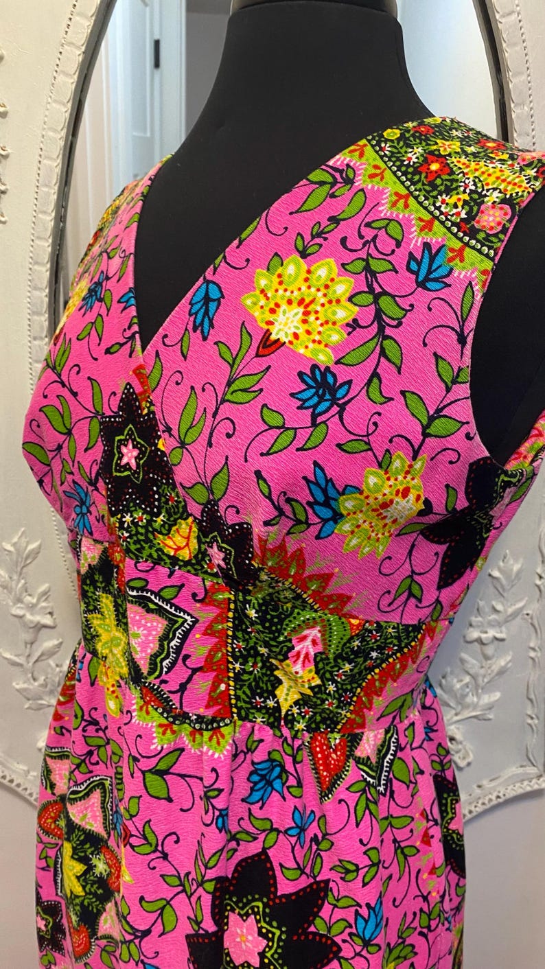 May include: A sleeveless pink dress with a floral print in shades of green, blue, yellow, red, and black. The dress has a V-neckline and a fitted bodice.