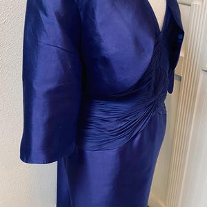 May include: A royal blue dress with a matching jacket. The dress has a fitted bodice with a gathered detail at the waist and a flowing skirt. The jacket has a shawl collar and three-quarter sleeves.