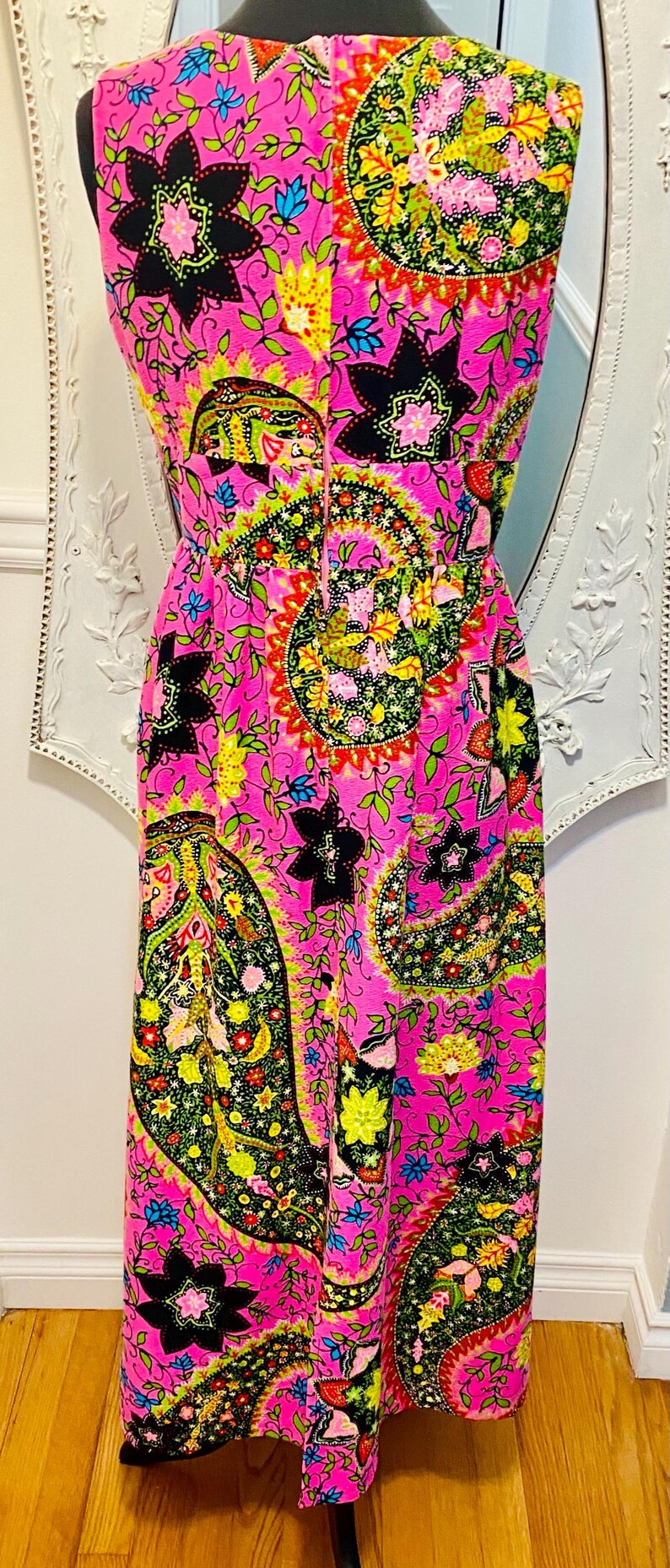 May include: A sleeveless maxi dress with a pink background and a colorful paisley pattern. The dress has a fitted bodice and a flowing skirt.