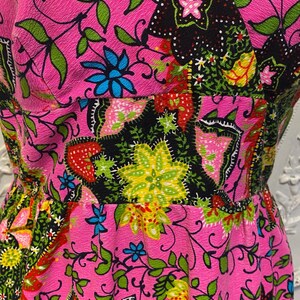May include: A pink dress with a floral print featuring black, green, yellow, red, and blue colors. The dress has a V-neckline and a fitted bodice.