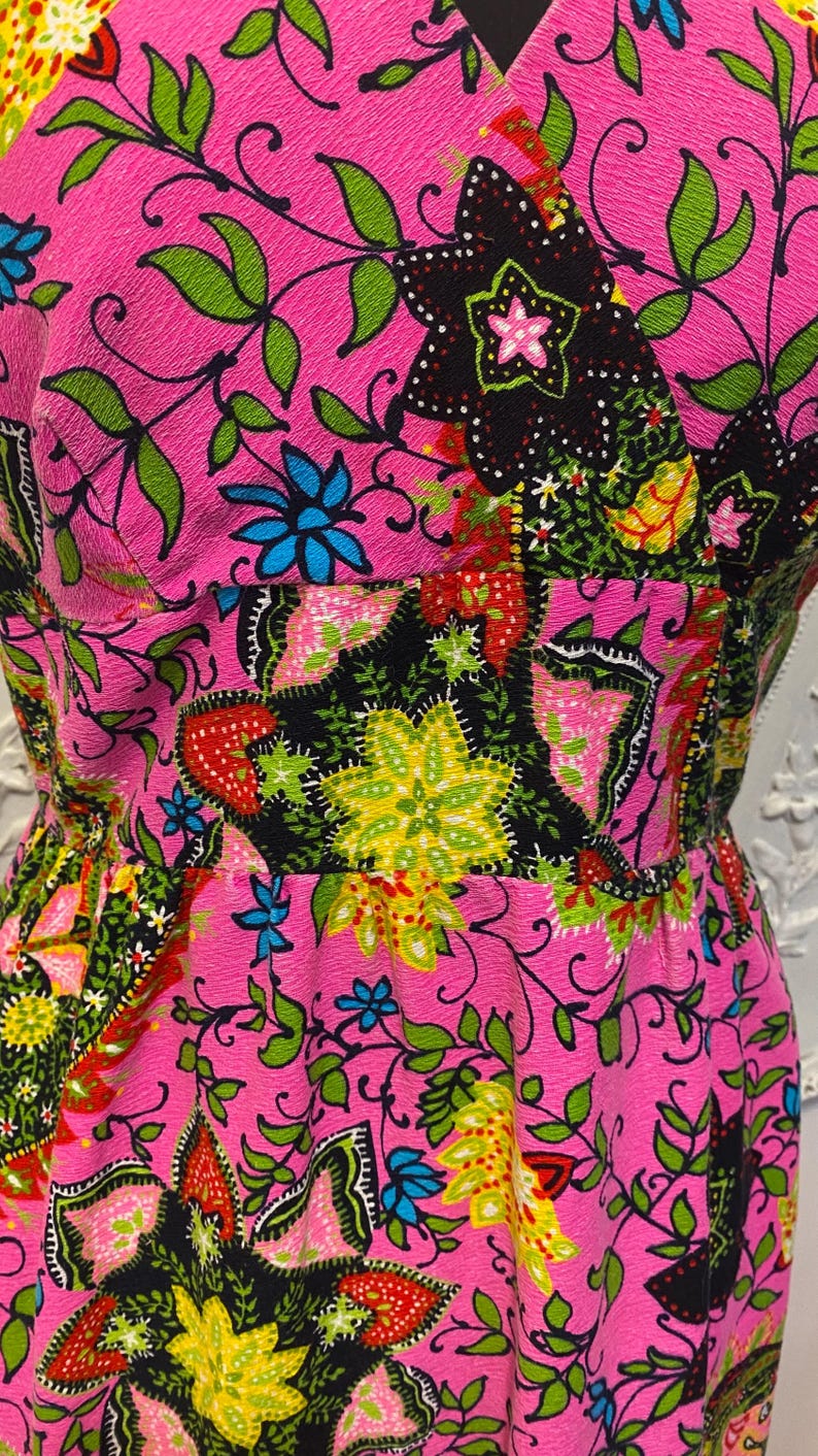 May include: A pink dress with a floral print featuring black, green, yellow, red, and blue colors. The dress has a V-neckline and a fitted bodice.