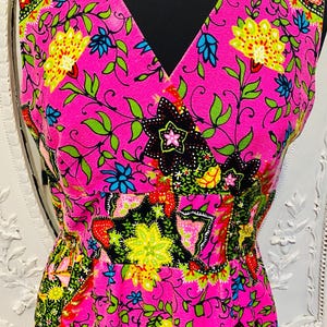 May include: A pink sleeveless dress with a V-neckline and a floral print. The dress has a fitted bodice and a flowing skirt.