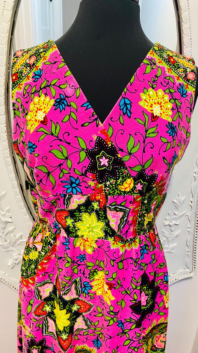 May include: A pink sleeveless dress with a V-neckline and a floral print. The dress has a fitted bodice and a flowing skirt.