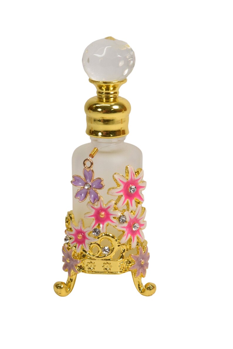 May include: A clear glass bottle with a gold top and a decorative stand. The stand is adorned with pink and purple flowers with gold accents and rhinestones.