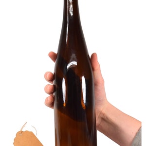 Puede incluir: Una botella de vidrio marr&oacute;n con un tap&oacute;n de corcho. La botella est&aacute; siendo sostenida por una mano.