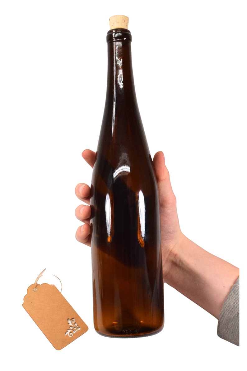 Puede incluir: Una botella de vidrio marr&oacute;n con un tap&oacute;n de corcho. La botella est&aacute; siendo sostenida por una mano.