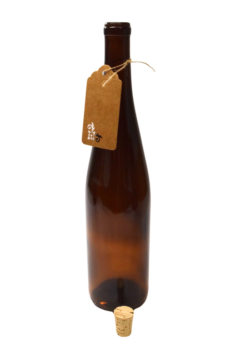 Puede incluir: Una botella de vidrio marr&oacute;n con un tap&oacute;n de corcho y una etiqueta de papel marr&oacute;n atada alrededor del cuello. La etiqueta tiene un dise&ntilde;o floral blanco.