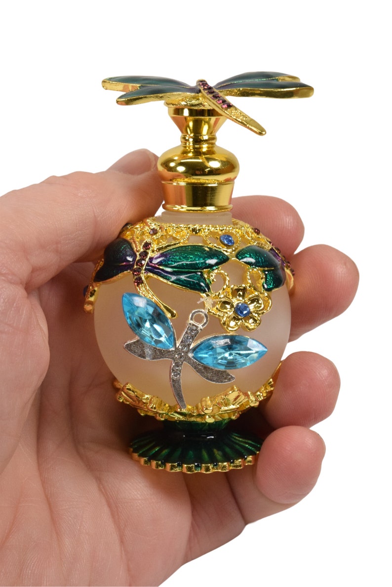May include: A gold and green glass perfume bottle with a dragonfly design. The bottle has a frosted glass body and a gold metal cap with a dragonfly on top. The bottle is decorated with blue and green enamel.