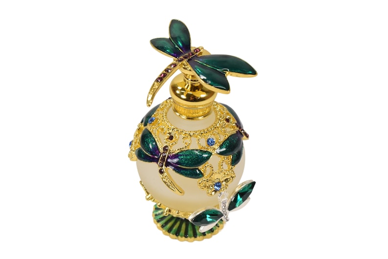 May include: A gold and green glass perfume bottle with a dragonfly design. The bottle has a frosted glass body and a gold metal cap with a dragonfly on top. The bottle is decorated with green and purple enamel and rhinestones.
