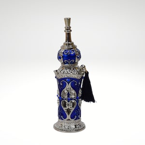 Op de afbeelding: Een decoratieve fles in zilver en blauw met een kwast. De fles heeft ingewikkelde ontwerpen en een zilveren dop.