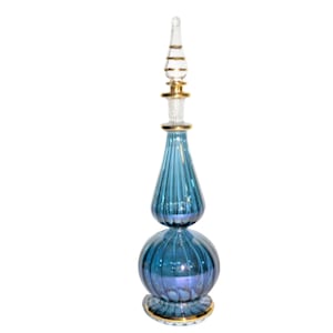 May include: A tall, blue glass bottle with a gold-trimmed stopper. The bottle has a bulbous shape with a narrow neck and a wide base. The bottle is decorated with vertical lines.