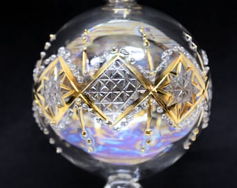 May include: A clear glass Christmas ornament with a gold and white geometric design. The ornament has a iridescent finish and a small loop at the top for hanging.