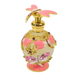 May include: A pink and gold glass perfume bottle with a dragonfly design. The bottle has a frosted glass body and a gold metal cap with a pink dragonfly on top.