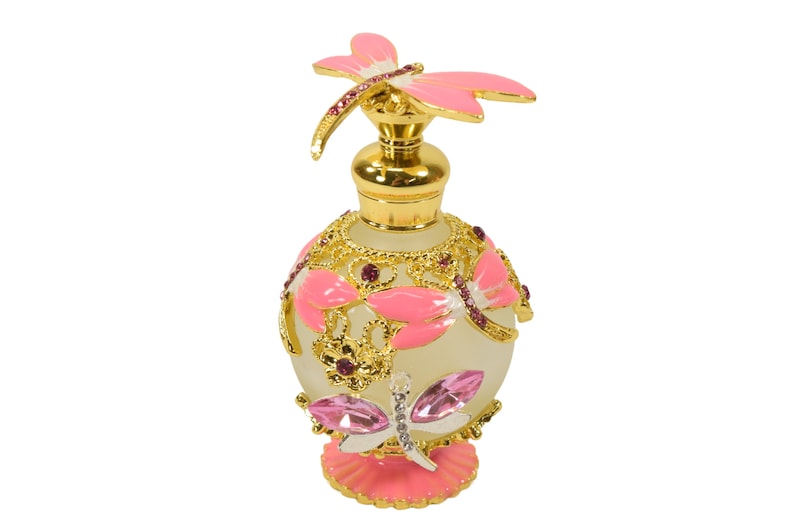 May include: A pink and gold glass perfume bottle with a dragonfly design. The bottle has a frosted glass body and a gold metal cap with a pink dragonfly on top.