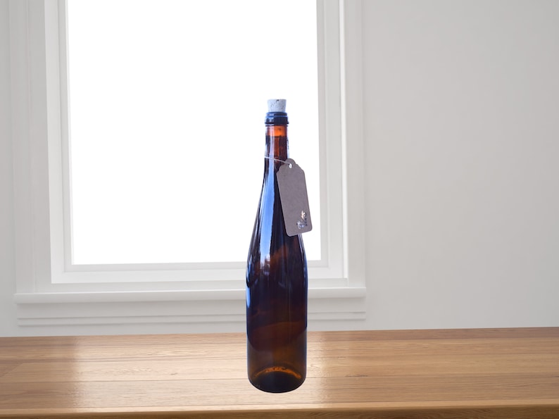 Puede incluir: Una botella de vidrio marr&oacute;n oscuro con un tap&oacute;n de corcho y una etiqueta de papel marr&oacute;n. La botella est&aacute; sobre una superficie de madera.