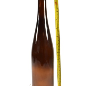 Puede incluir: Una botella de vidrio marr&oacute;n con un tap&oacute;n de corcho y una etiqueta de papel marr&oacute;n. La botella mide 28 cm de alto y est&aacute; al lado de una cinta m&eacute;trica amarilla.