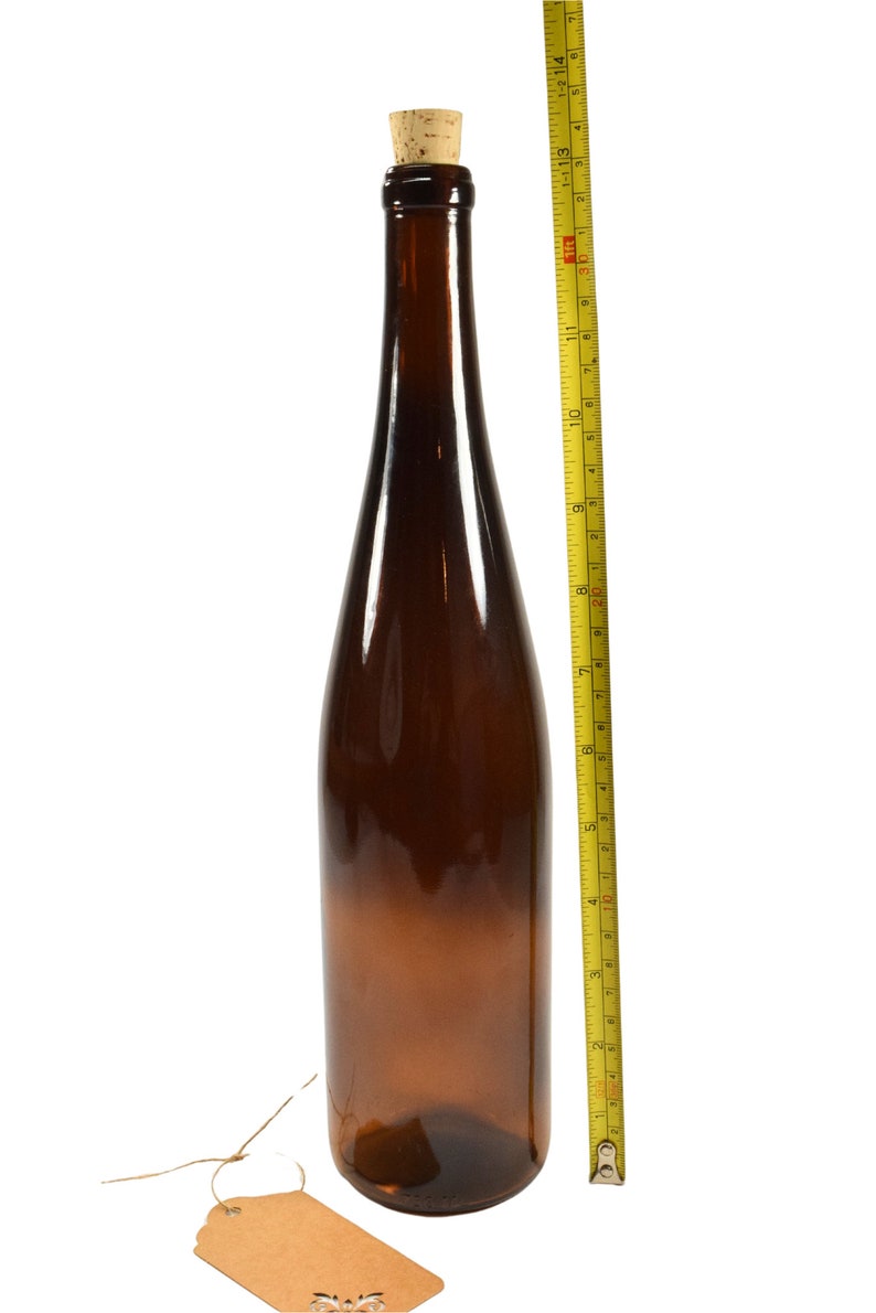 Puede incluir: Una botella de vidrio marr&oacute;n con un tap&oacute;n de corcho y una etiqueta de papel marr&oacute;n. La botella mide 28 cm de alto y est&aacute; al lado de una cinta m&eacute;trica amarilla.