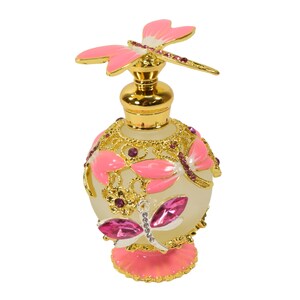 May include: A gold and pink glass perfume bottle with a dragonfly design. The bottle has a clear glass body with gold accents and pink butterfly wings. The bottle is decorated with pink and purple rhinestones.