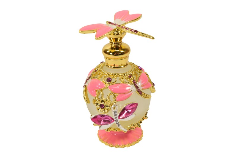 May include: A gold and pink glass perfume bottle with a dragonfly design. The bottle has a clear glass body with gold accents and pink butterfly wings. The bottle is decorated with pink and purple rhinestones.